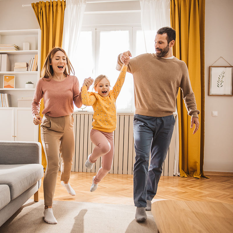 Happy family, mother, father and daughter jumping and playing at home
