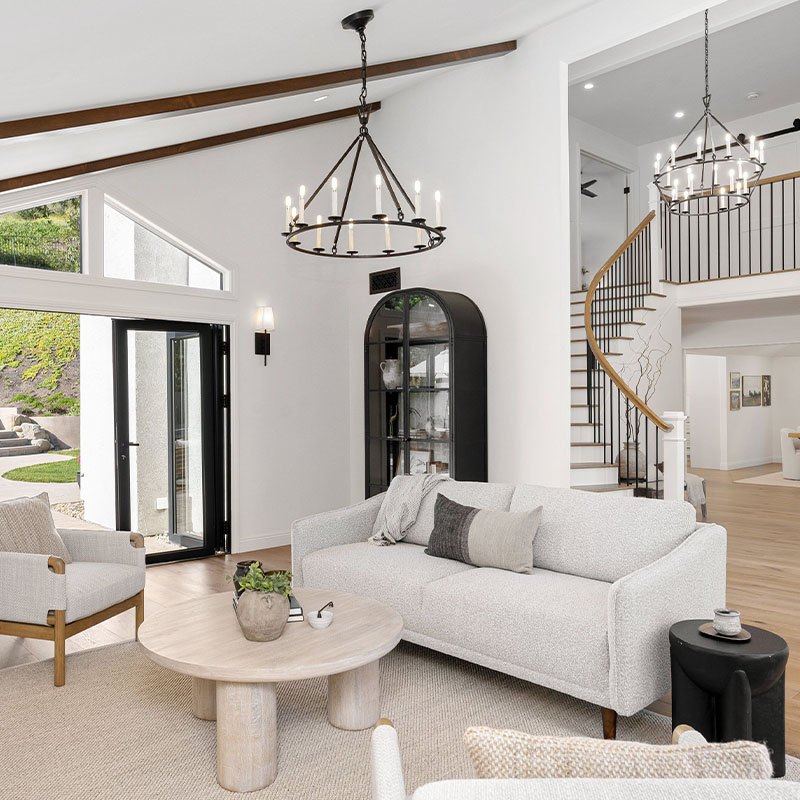 Modern living room with white furniture, wooden floor, and large windows o