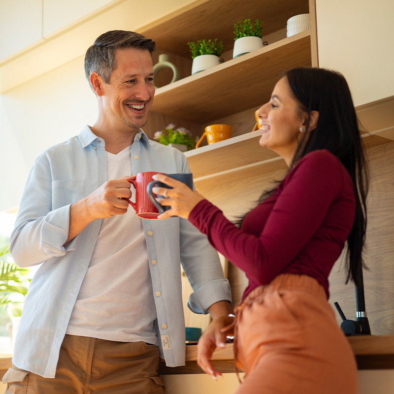 Happy couple smiling and toasting coffee mugs in their modern kitchen